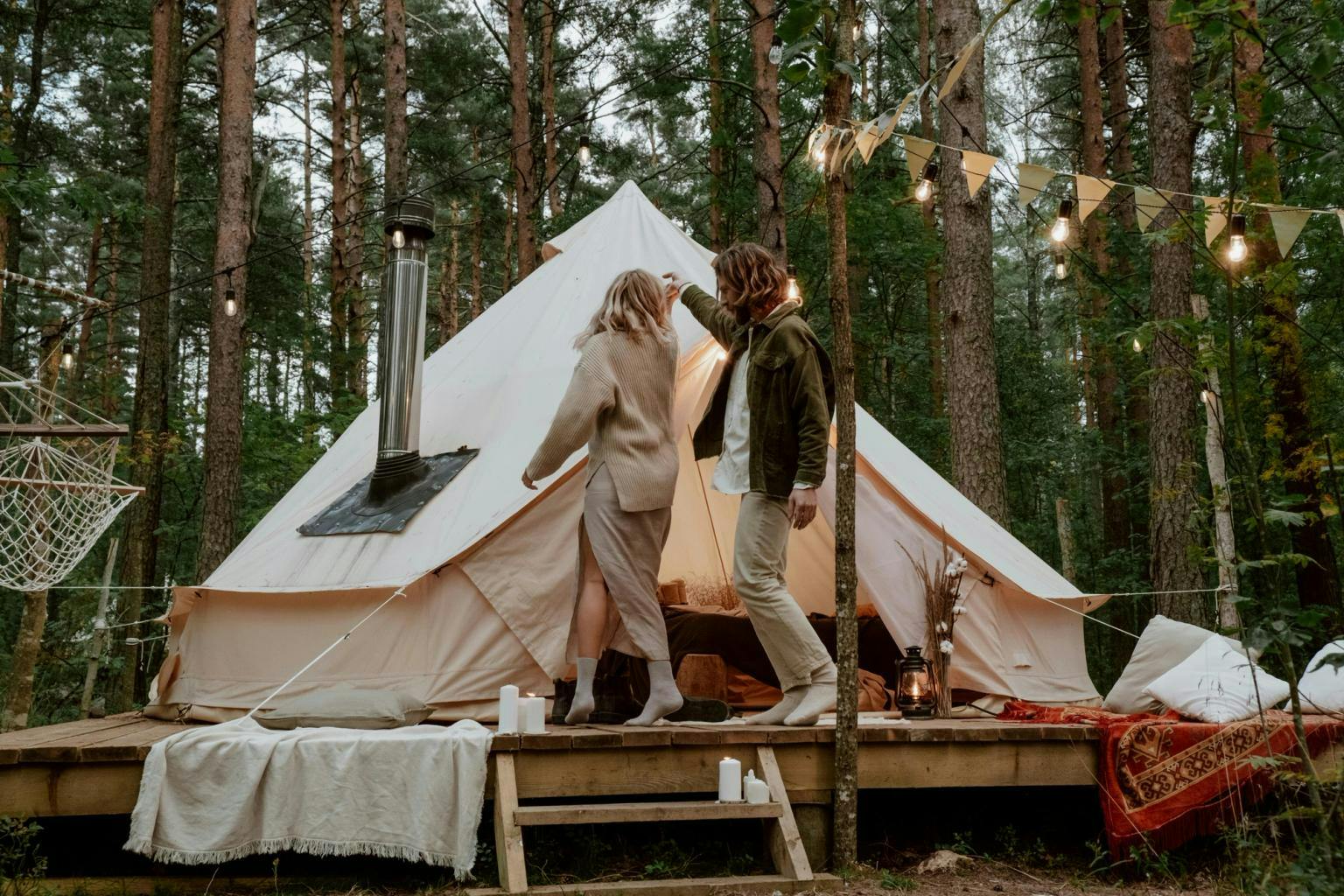 A couple enter a yurt style tent in a woodland surrounded by fairylights