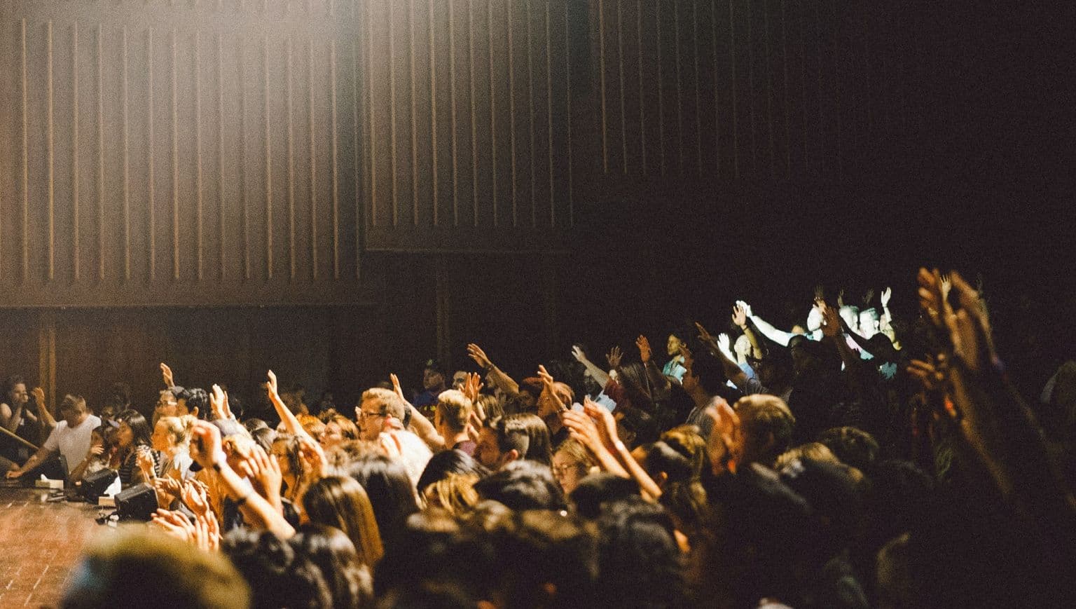 Shot of an audience in an auditorium with many raised hands, facing the stage.