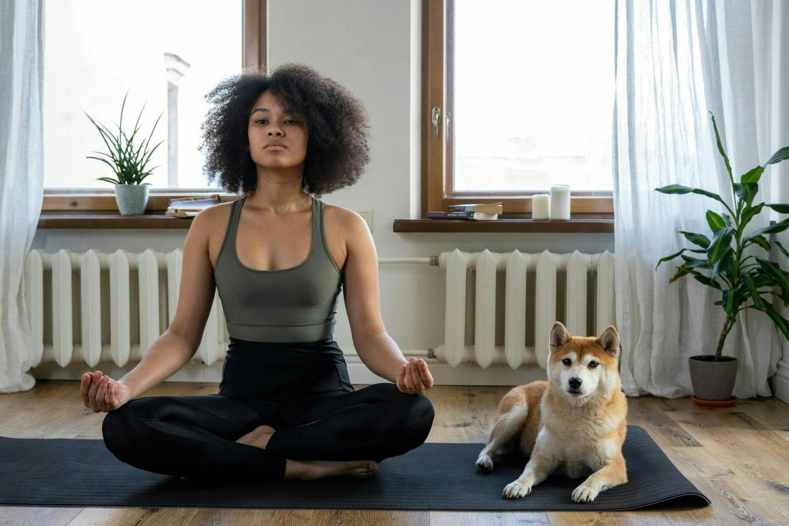 A woman sits on  a yoga mat crossed legged with her dog by her side