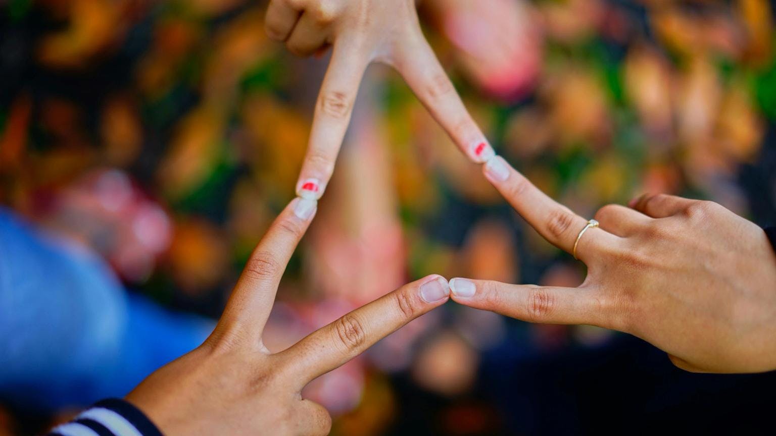 Three sets of hands with colourful nail polish join fingers together.