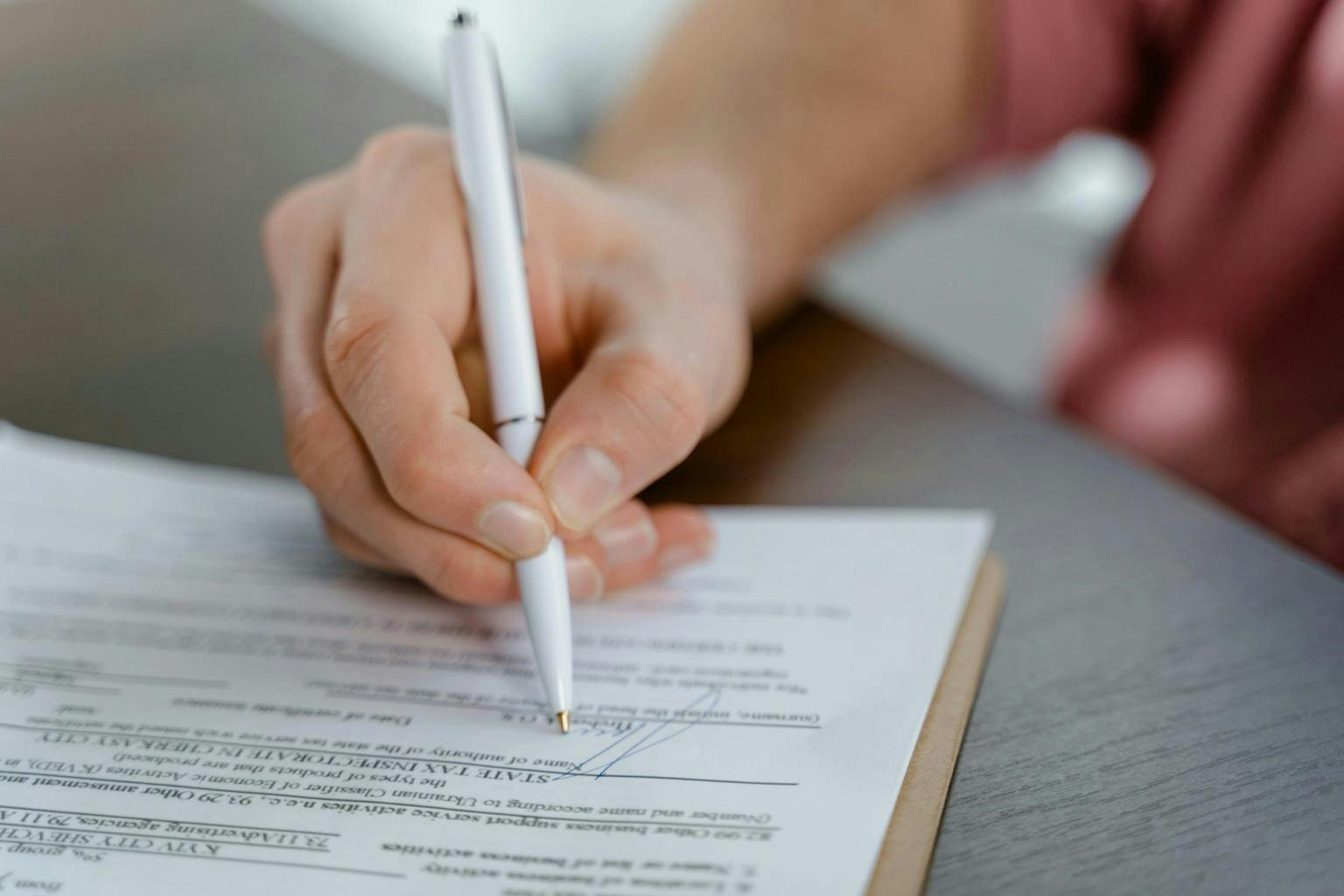 A hand holding a pen and signing a document