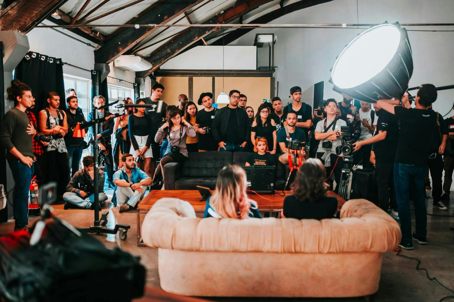 An audience gathered around two speakers on a sofa with their backs to the camera.