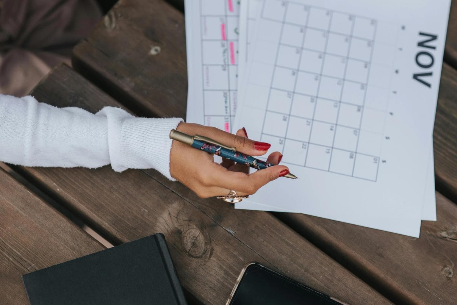 A woman's hand holds a pen as she reviews a calendar printed onto paper.