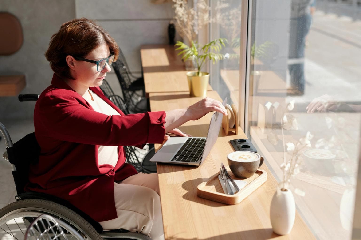 A woman sits in a wheelchair doing work on a laptop in the window of a working space.