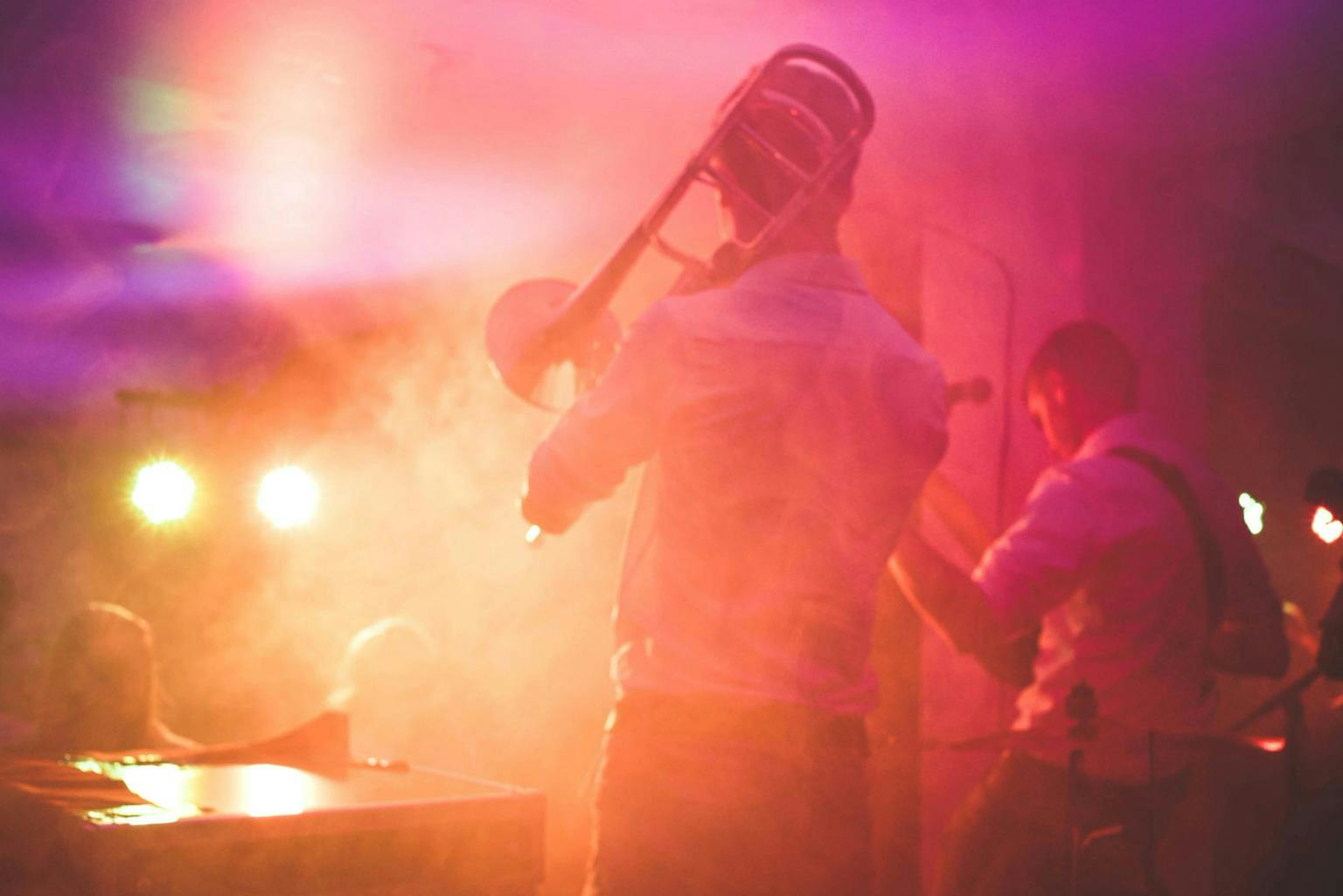 Jazz musicians play to an audience, lit with pink and gold lights