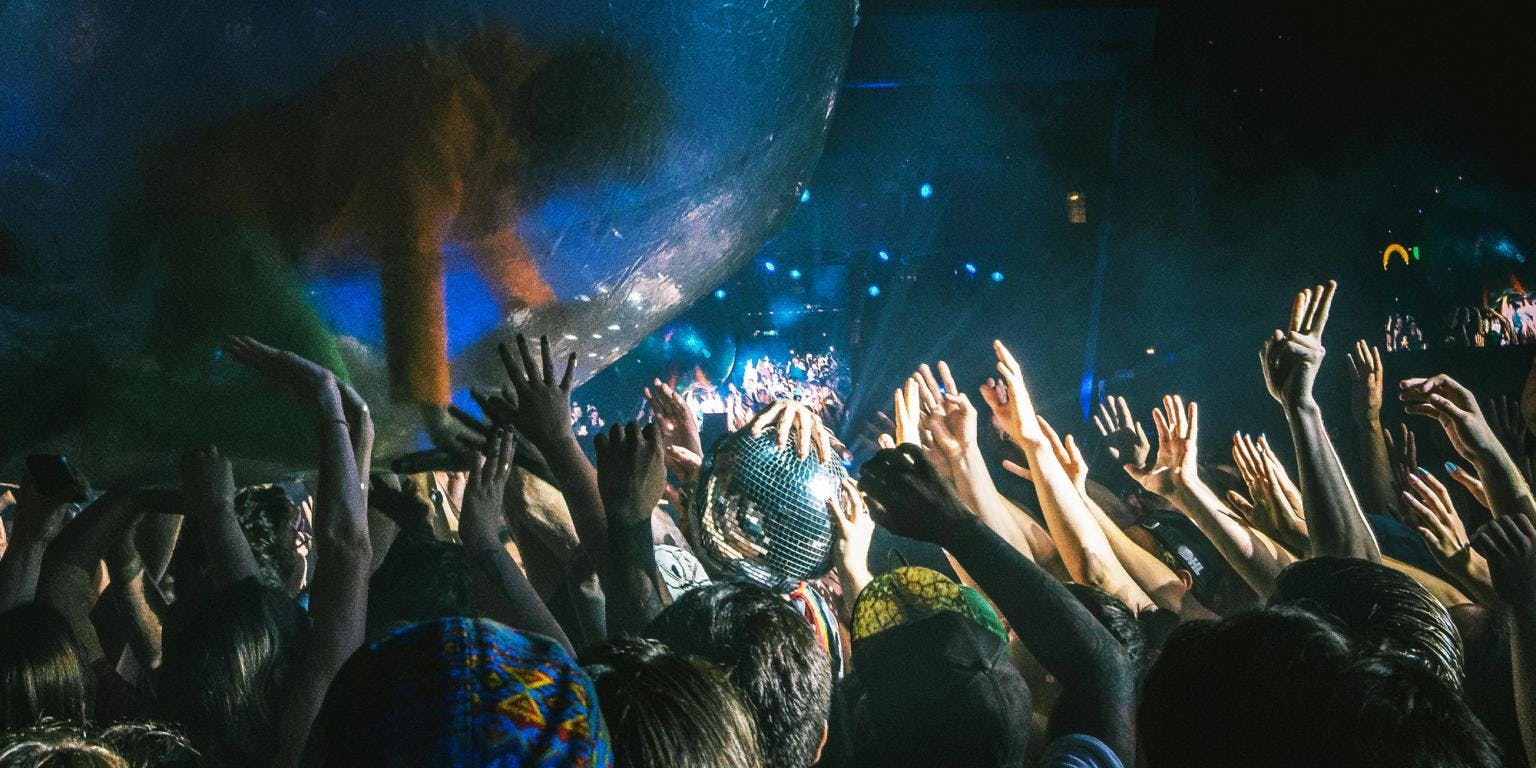 Members of an audience have their hands in the air and a disco hall casts light around the room