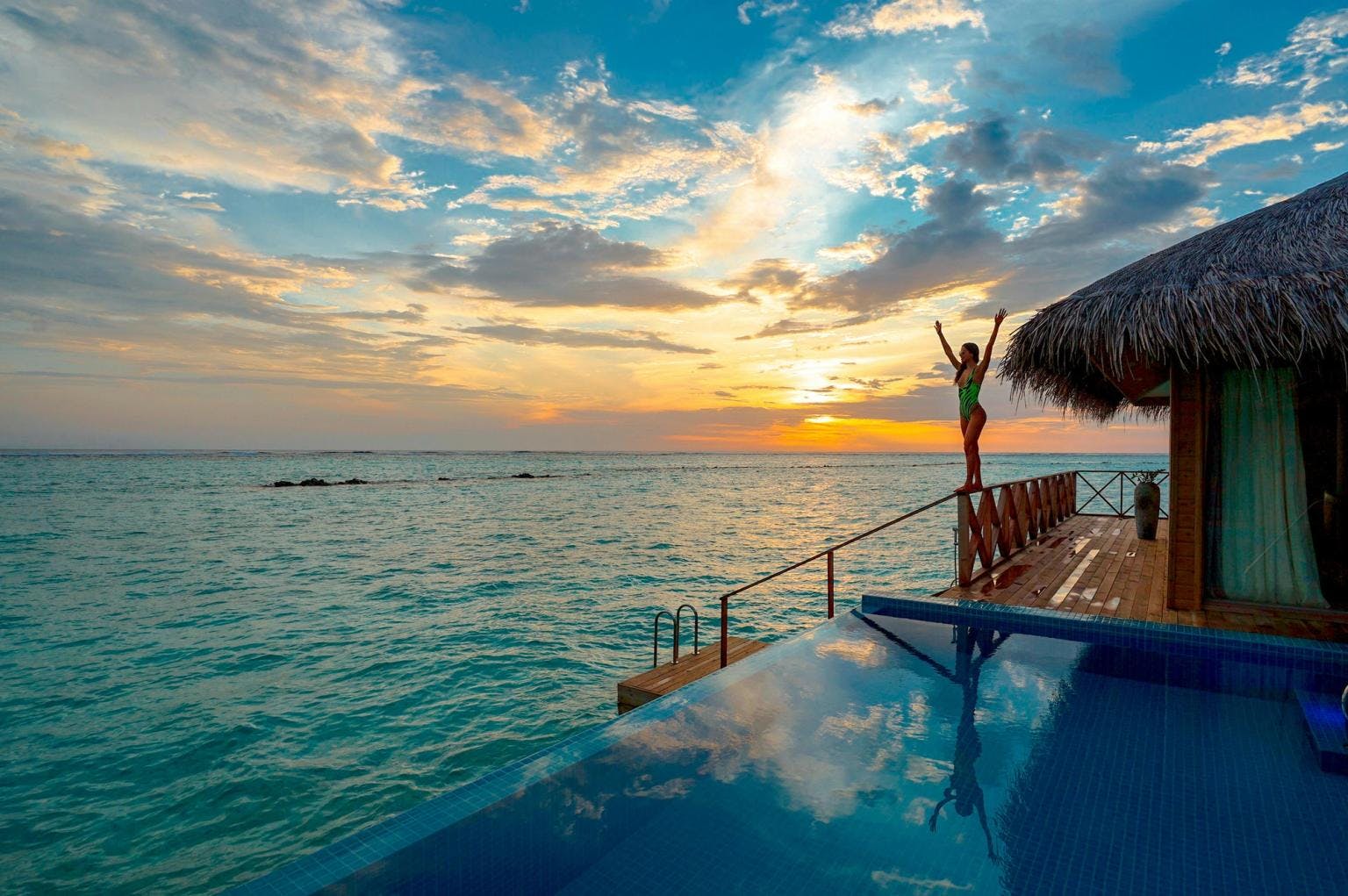 A woman walks along the side of a balcony over the ocean, next to an infinity pool