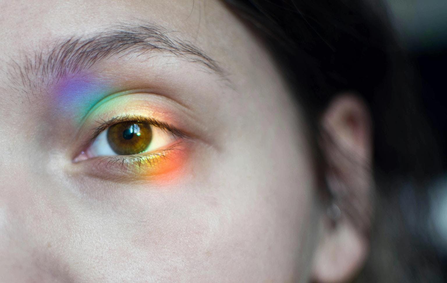 A close up of a woman's eye with a a rainbow prism of light shining on it