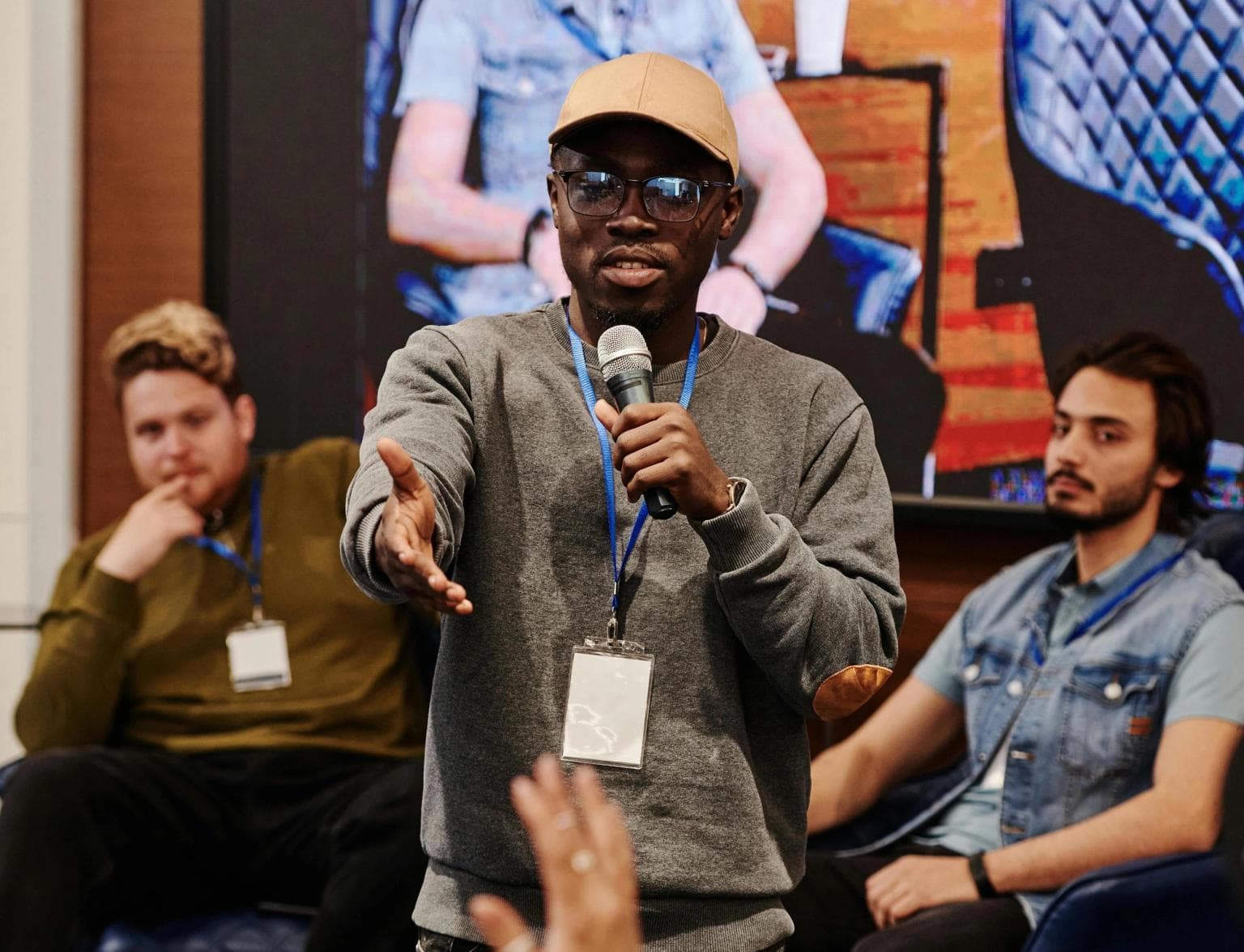 A panel host takes questions from the audience with two men sitting on stage behind him