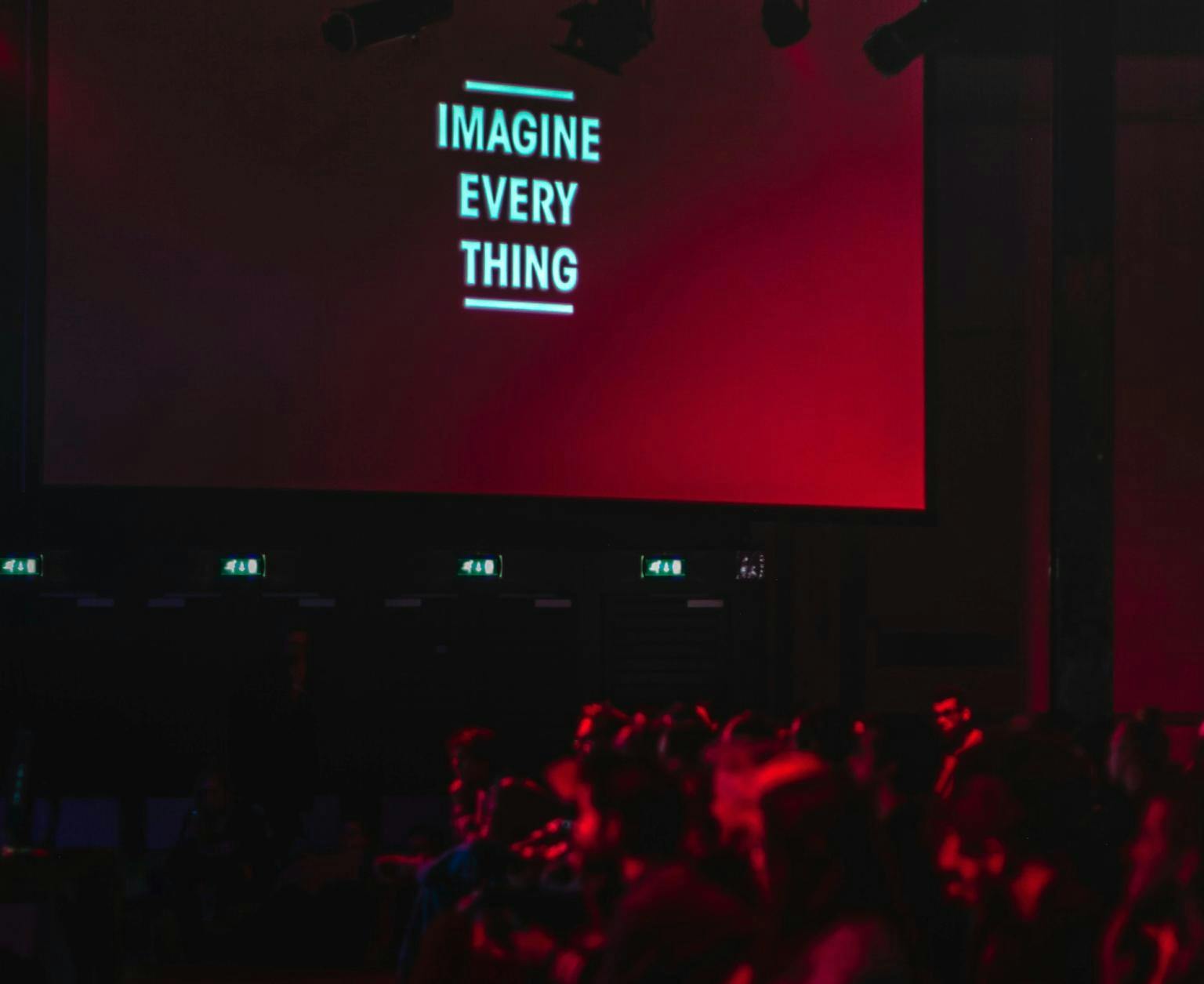 The words 'IMAGINE EVERY THING' show on a cinema screen with an audience visible in the screen light