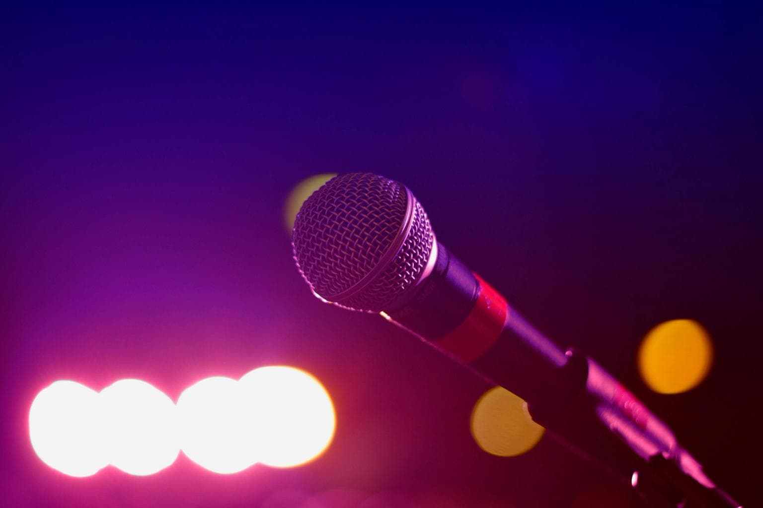 A close up of a microphone with blurred stage lights in the background.