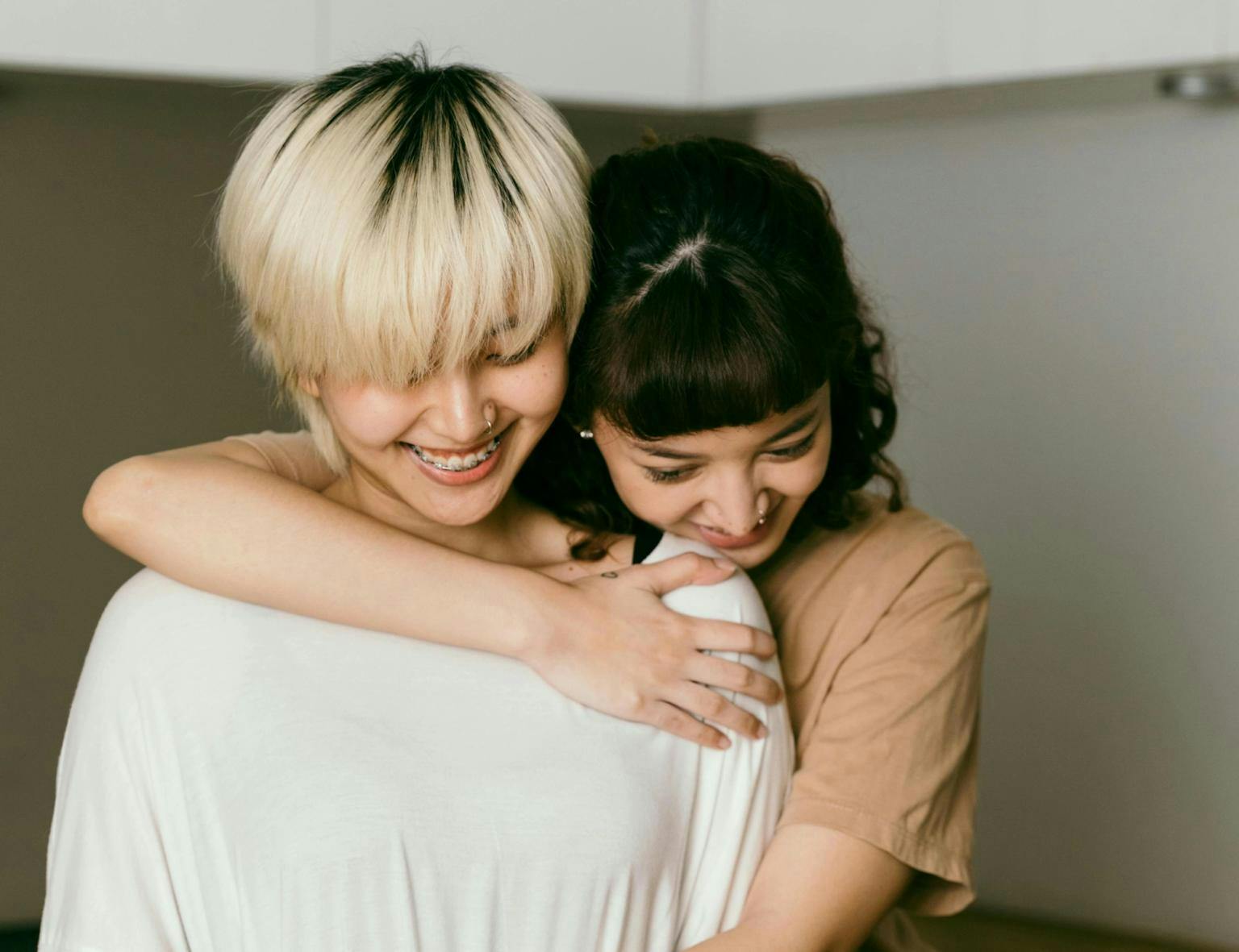 A woman hugs another woman from behind as they smile