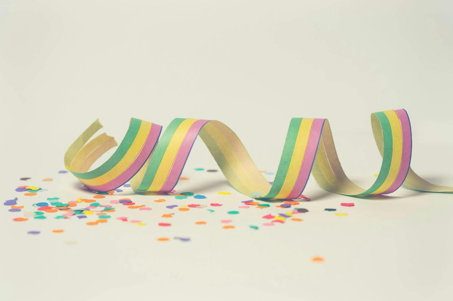 A rainbow party streamer and confetti against a plain backgroud.