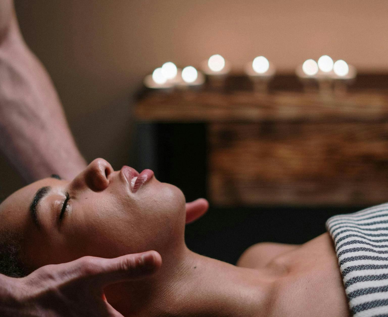 A woman is lying down having a massage with candles in the background