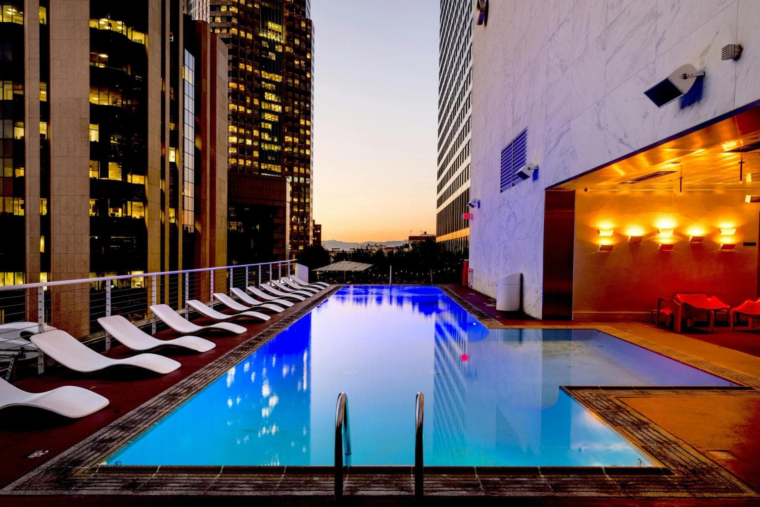 A hotel swimming pool sits in front of a backdrop of high rise hotels at dusk