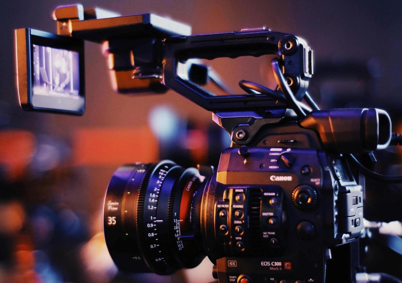 A film camera is in the foreground and on the display screen. you can see it's filming someone giving a talk on a laptop