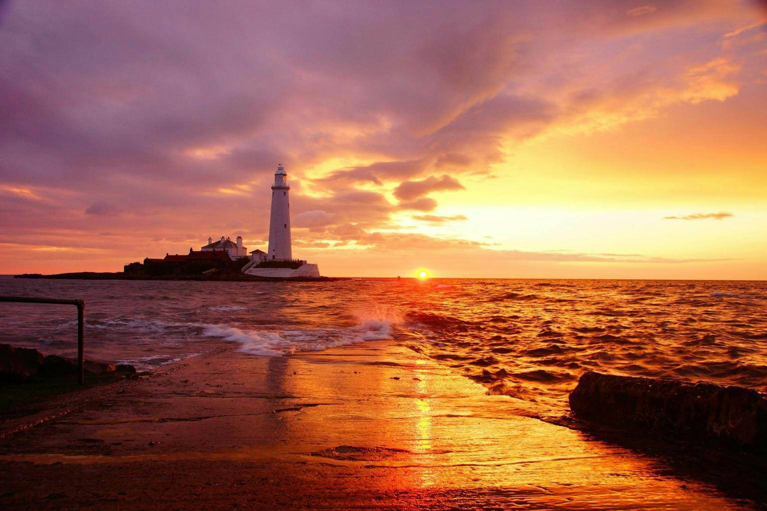 A lighthouse with an orange sunset sites on a small island 