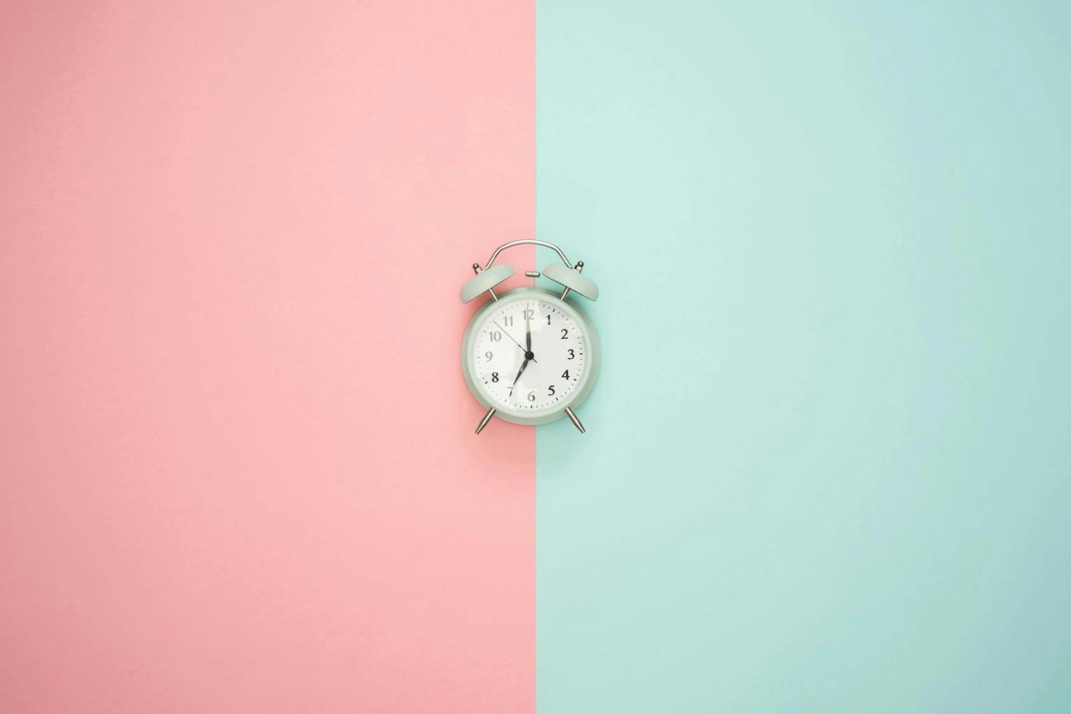 An alarm clock sits against a turquoise and pink background