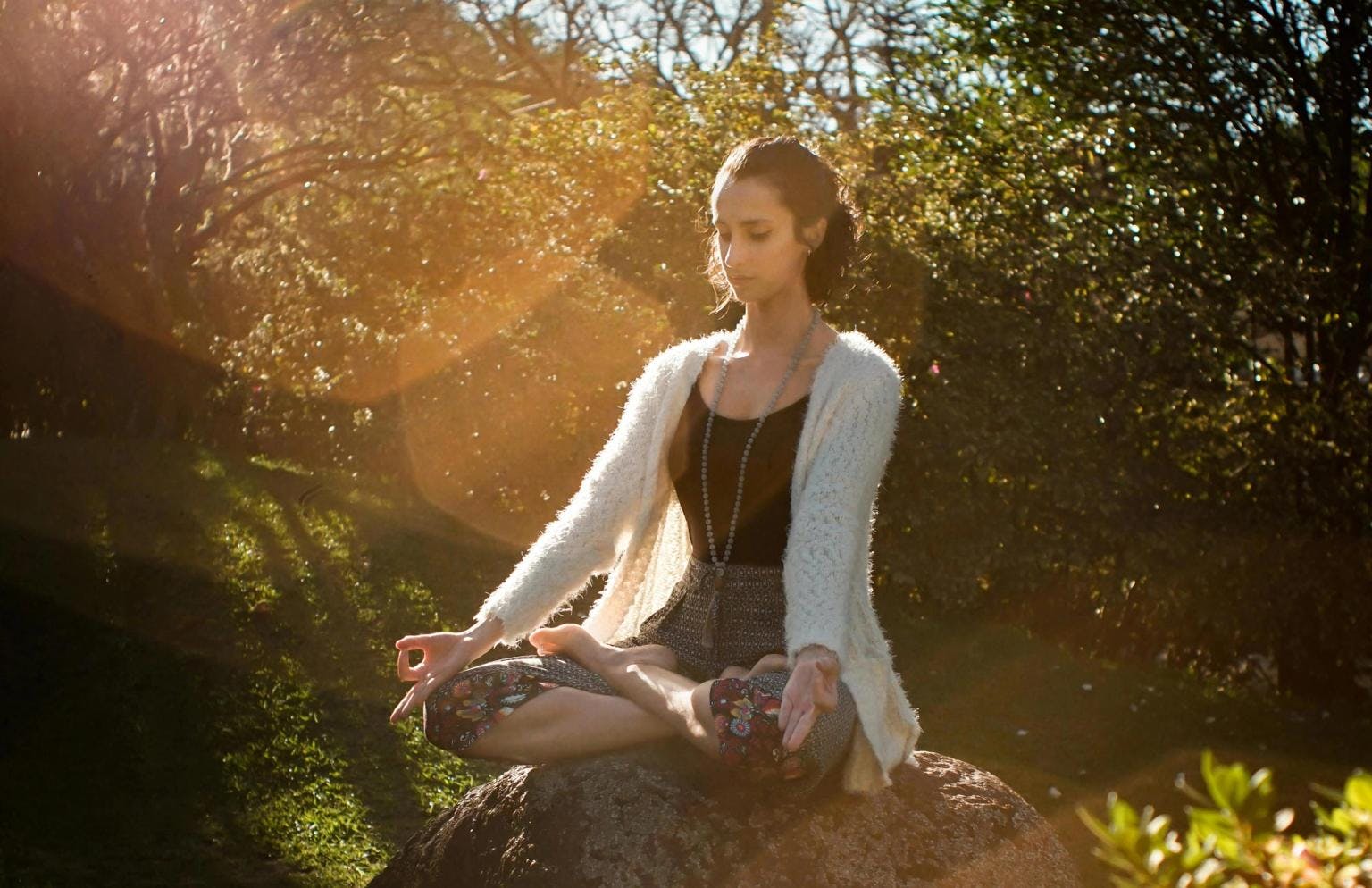 A woman sits on a rock at golden hour, meditating