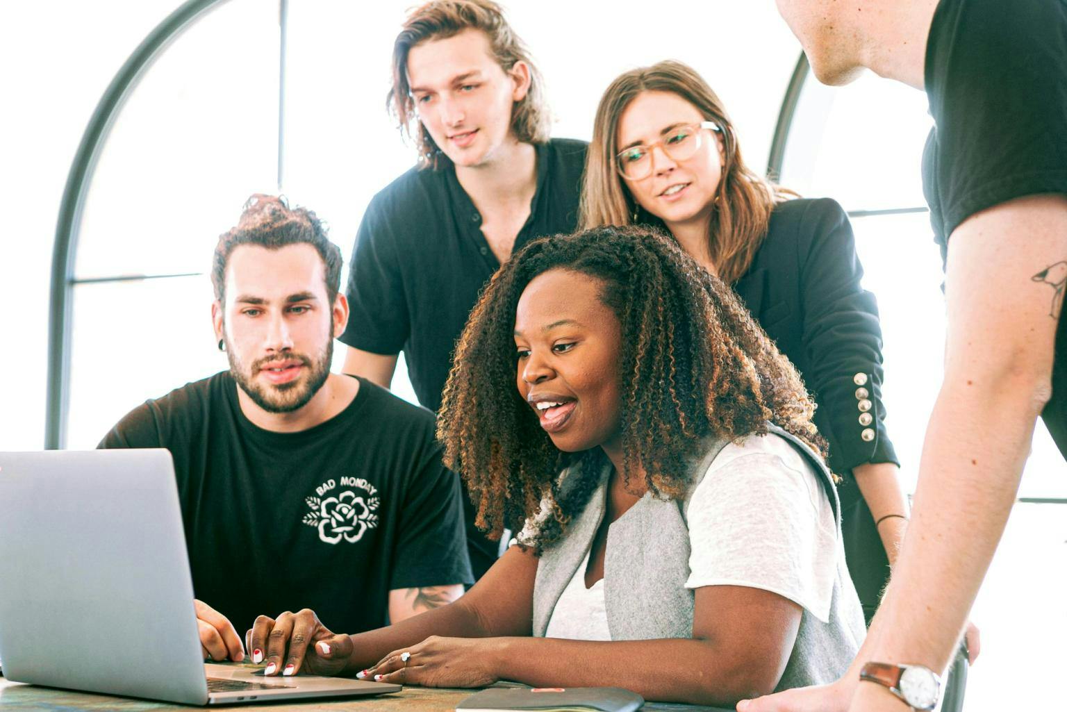 A group of young professionals huddle around laptop together, looking engaged.