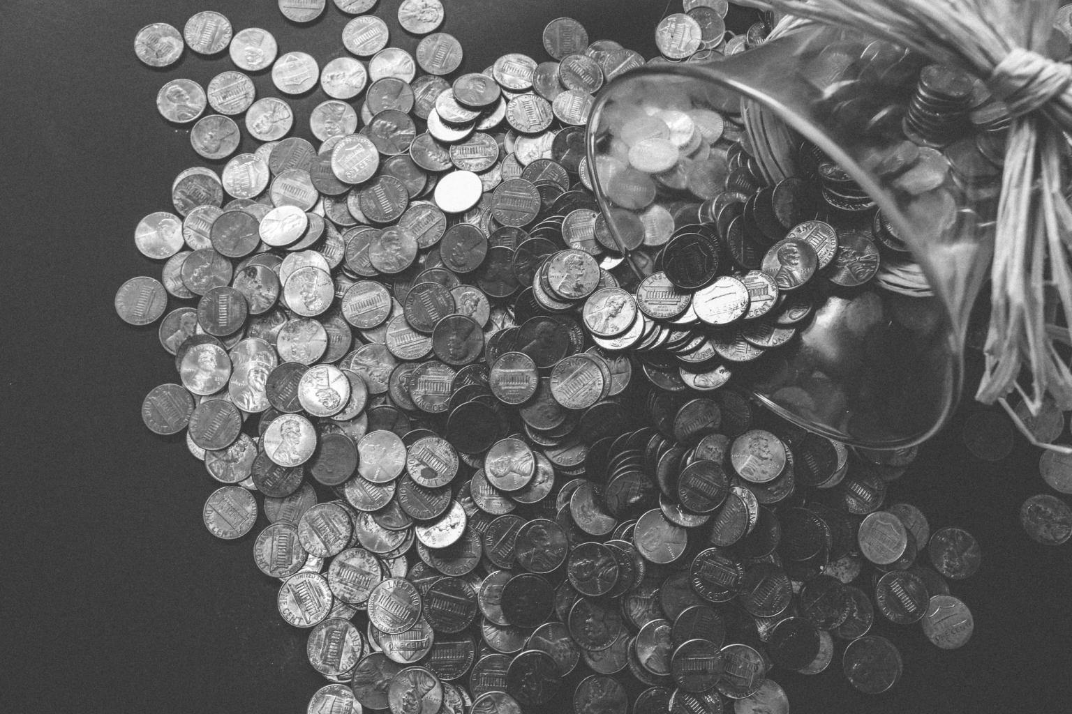 A black and white image of a pile of coins spilled from a glass vessel.