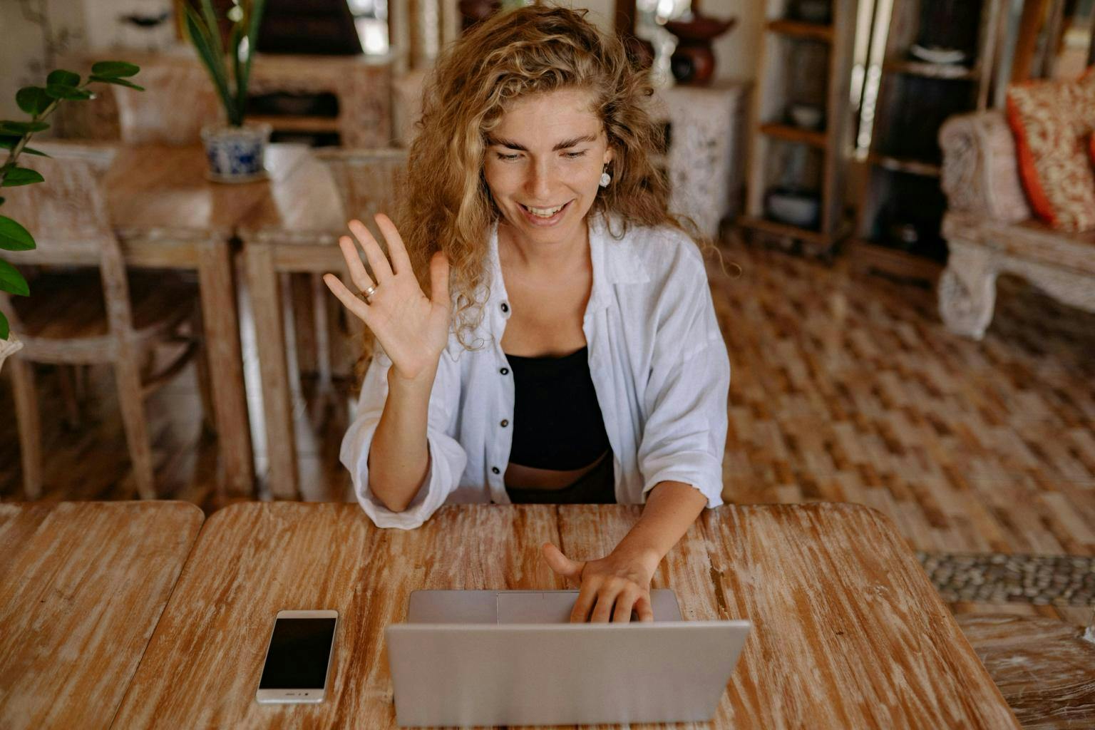 A woman on a laptop waves hello to the person she is talking to