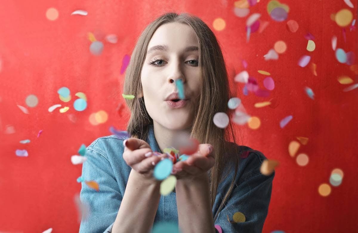 A woman blows confetti towards the camera