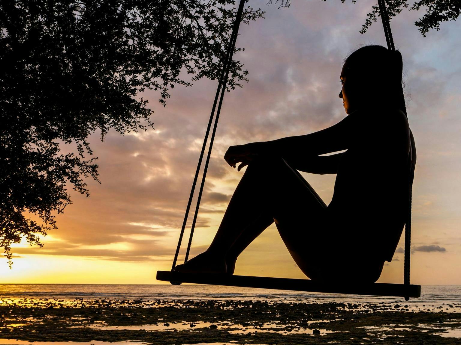 A silhouette of a woman sitting on a swing at sundown looking over the ocean
