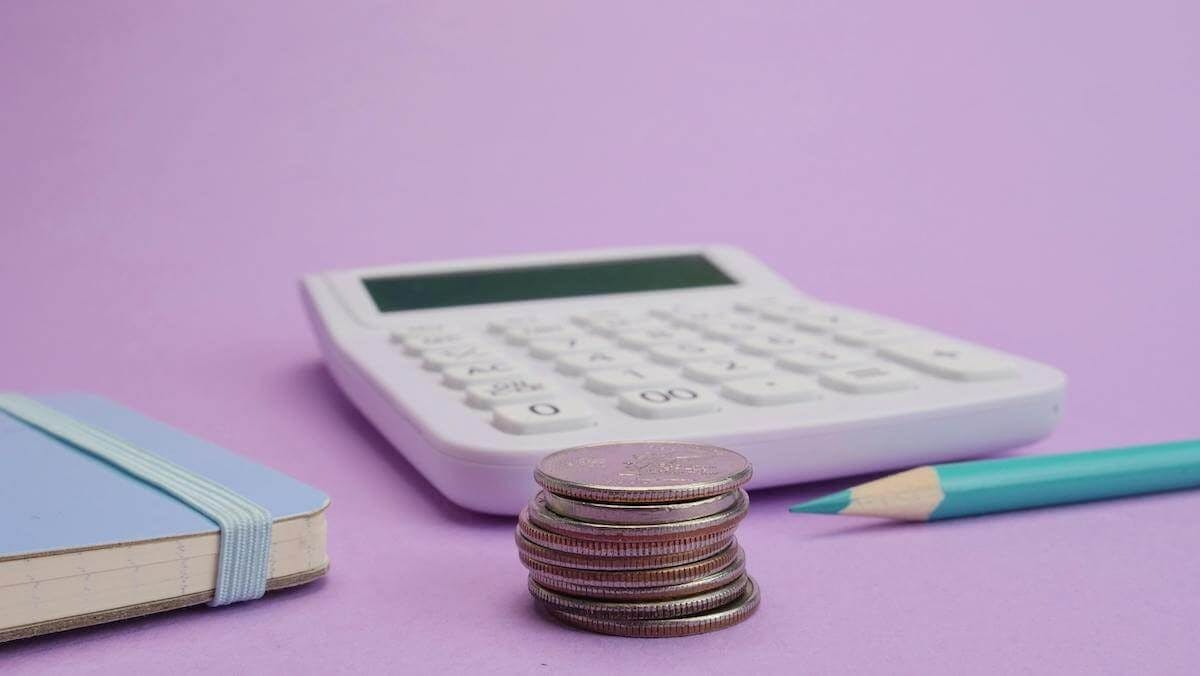 A calculator sits next to a pencil, some coins and a notepad