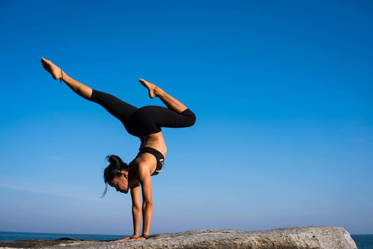 Woman does handstand yoga pose on rock against blue sky
