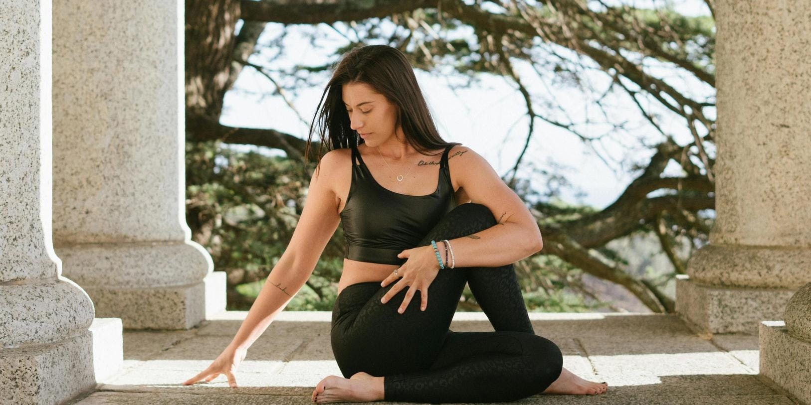 Woman sits in a yoga posevbetween stone pillars in front of a tree