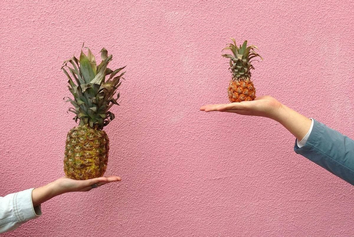 Two hands each hold up a a pineapple, one larger, one smaller, to represent weighing things up