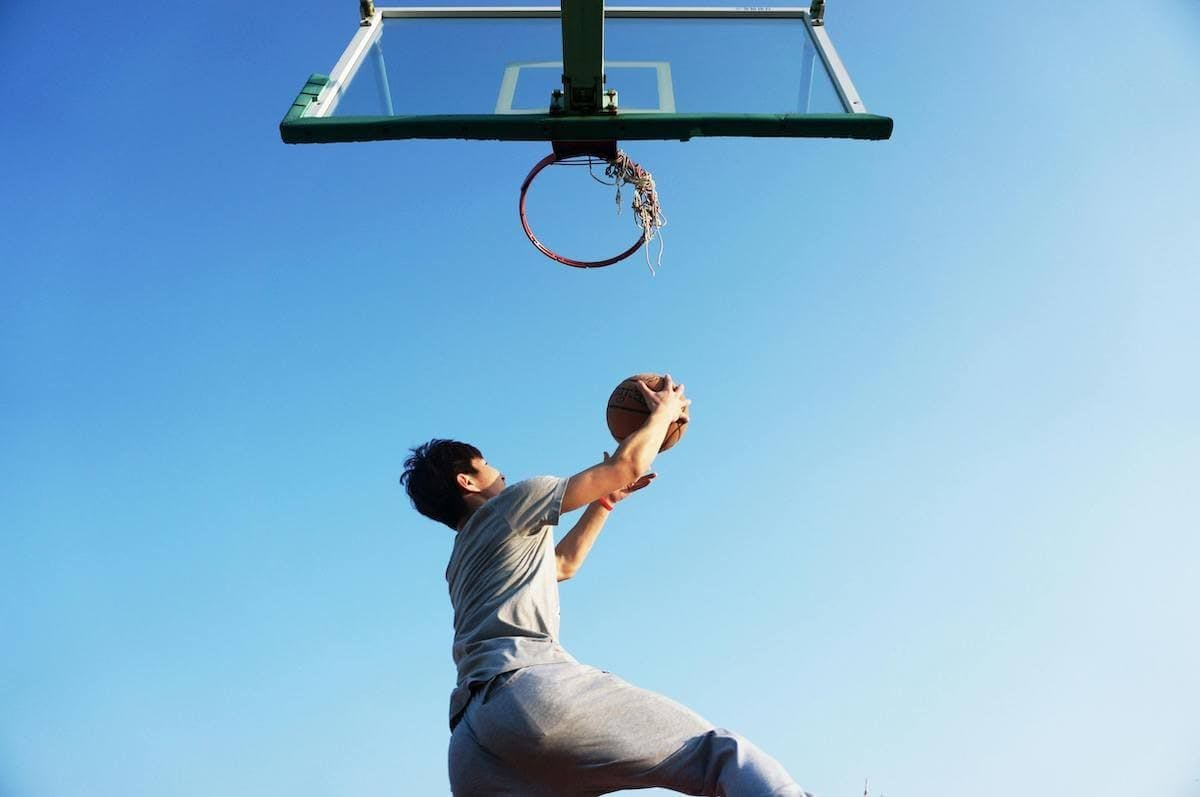 A man jumps toward a basketball hoop to shoot against a blue sky